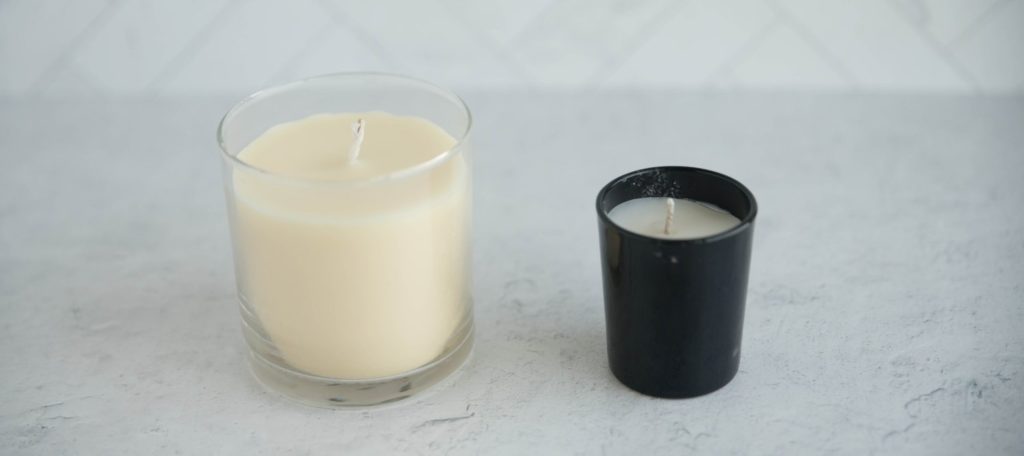 Honey Play Box Rose Mini Massage Candle. Image shows the Honey Play Box Massage Candle next to a regularly-sized candle. The Honey Play Box Massage Candle clearly looks small compared to the large candle next to it. 