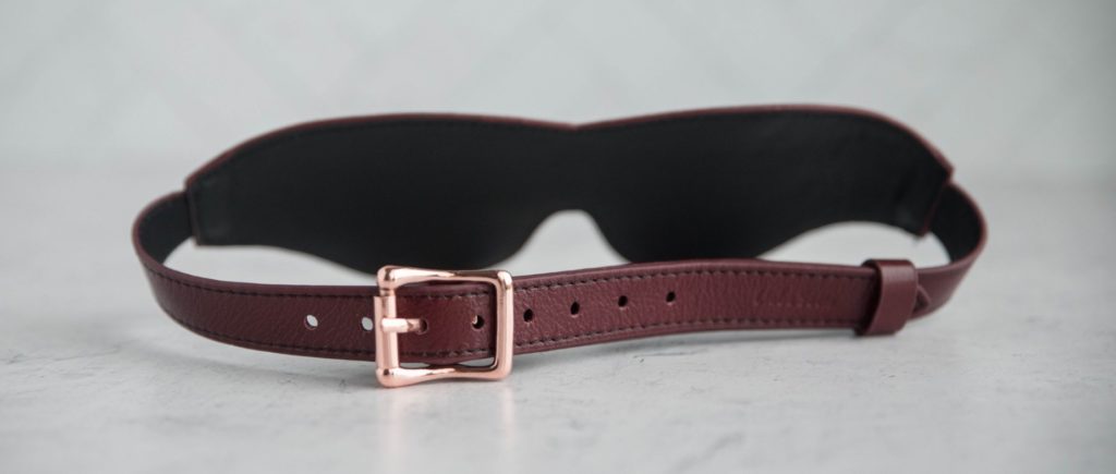 An image shows the backside of the leather blindfold which displays the buckle closure