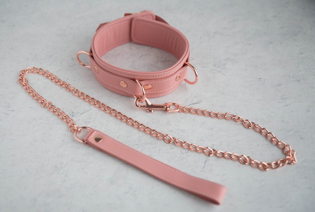 Liebe Seele Pinku Pink Collar and Leash. Image shows the collar sitting on a surface with all three D-rings expanded from the collar. The leash's clip is clipped onto the front D-ring of the collar.