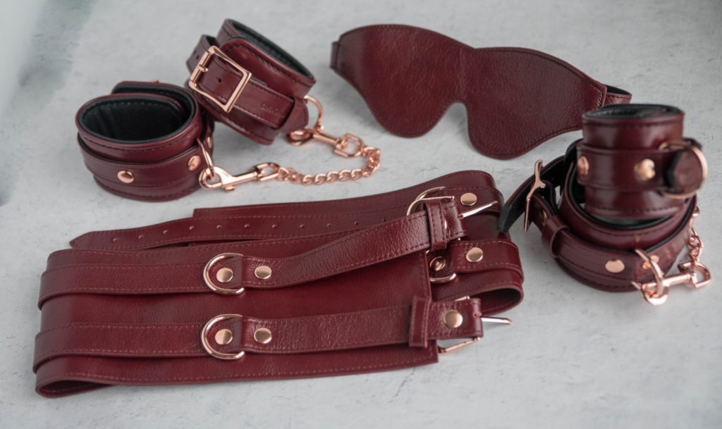 Liebe Seele Wine Red Cuffs review. The full Wine Red set of bondage items. Picture shows the blindfold, the wrist cuffs, the ankle cuffs, and the waist bondage belt. All in Wine Red.