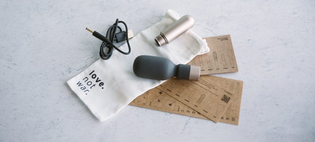 Love Not War Koi review: The Love Not War Koi sitting out among everything that comes with the wand massager. There's the instruction manual printed on plain cardboard, the drawstring storage pouch, and the charging cable.