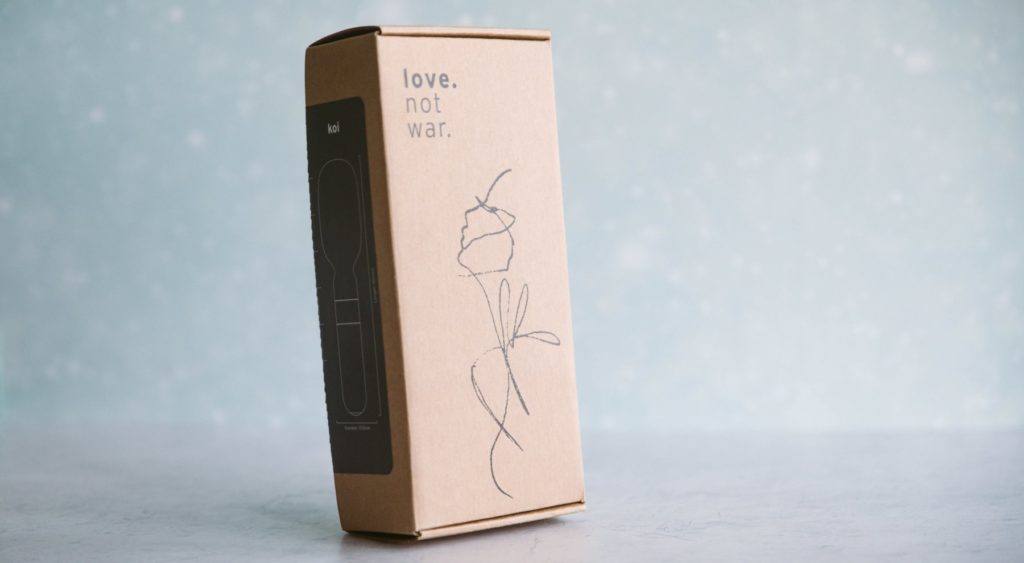 Love Not War Koi review: The Koi is sitting inside of its cardboard packaging. The packaging looks minimalist, and all of it is cardboard and recyclable. There is a sticker on the outside of the packaging that explains the toy.