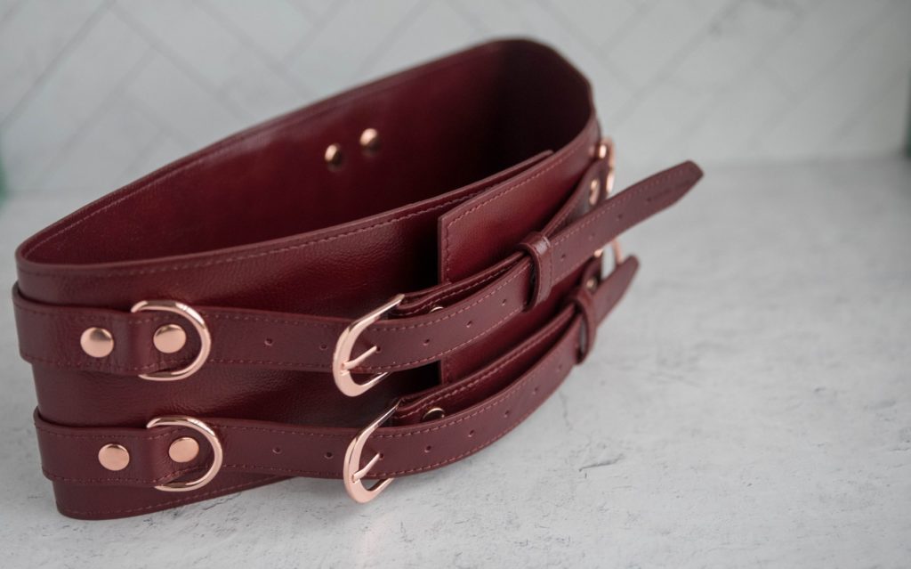 Liebe Seele Wine Red Waist Cuff Review: Close-up of the rose gold hardware on the Waist Cuffs. The rivets, D-rings, and fasteners all match and stand out against the wine red leather.