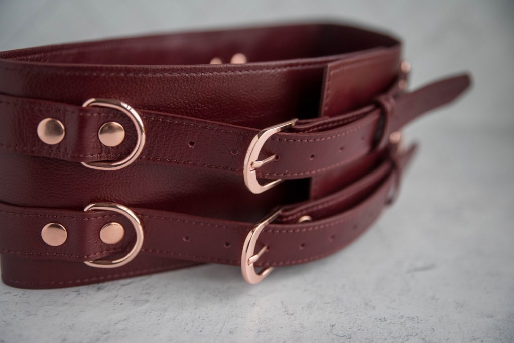 Liebe Seele Wine Red Waist Cuff Review: Close-up of the rose gold hardware on the Waist Cuffs. The rivets, D-rings, and fasteners all match and stand out against the wine red leather.