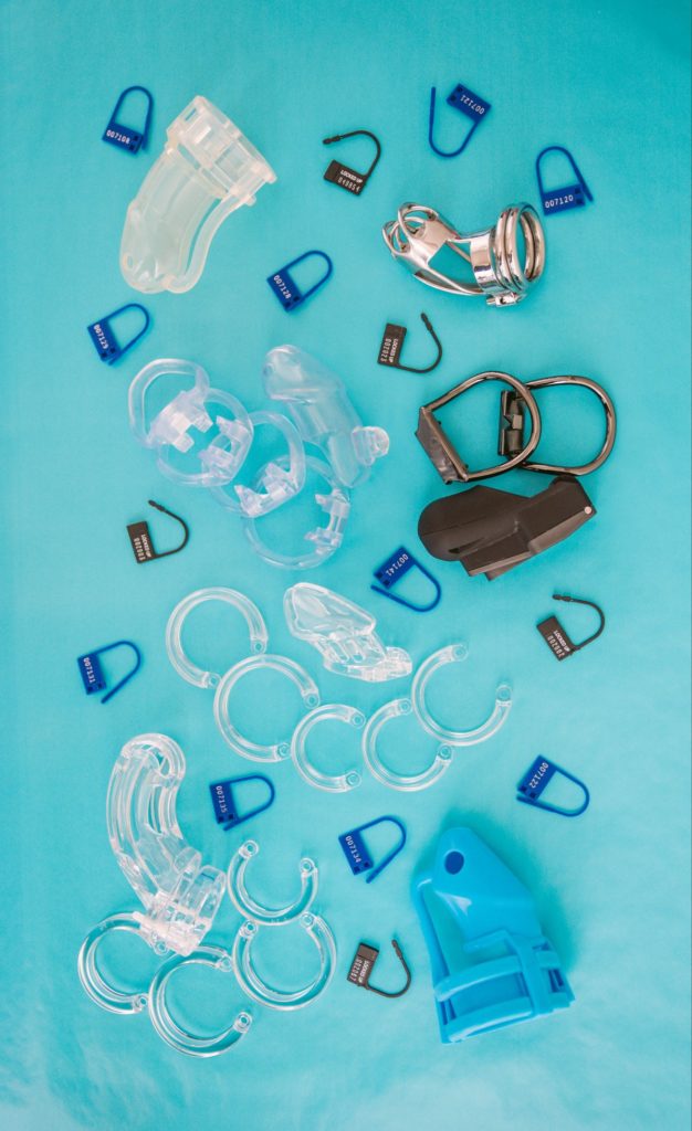 A bunch of chastity cages and plastic, one-time cut-off locks arranged nicely on a blue background for my step-by-step chastity scene.