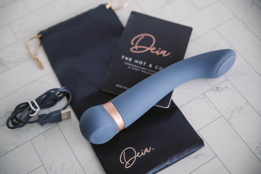 Image for my Deia Hot and Cold review. Includes everything that comes with the vibrator. The photo shows the Deia-branded storage bag, the charging cable, instruction manual, and the Deia Hot and Cold vibrator itself.