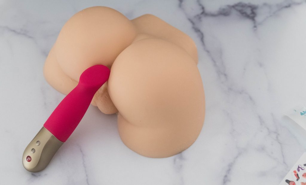 Image for my Sohimi Simon review. The tip of a pink vibrator is pressed up against the entrance of the Sohimi Simon. This showcases the size of the Sohimi (noticeably larger than the vibrator but not life-size).