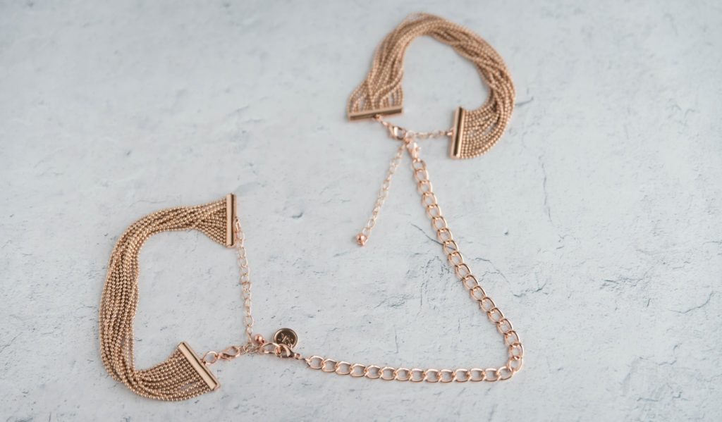 The two bracelets are laid out on a flat surface. The two bracelets are connected to one another via the included chain with the clasps. This shows how they all connect together. Secret Kisses Luxe Gold Bracelet Cuffs Review image.