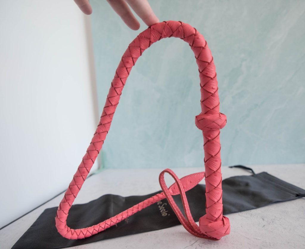 I hold the Liebe Seele Angel's Kiss Whip upright. The whip is clearly folded into thirds, and it bends into these thirds without any pressure being applied to it because the material has a "memory" from being stored in the packaging. Image for Liebe Seele Angel's Kiss Whip review.