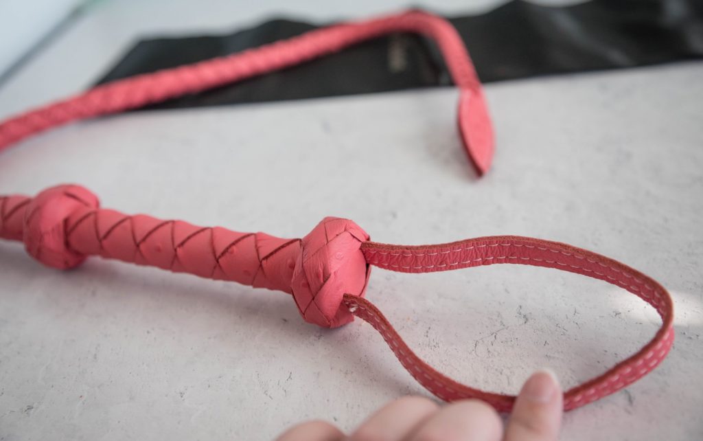 My finger pulls out the hanging/wrist loop at the base of the handle to showcase its wide size. The loop is clearly large enough to work for a wrist loop. Image for Liebe Seele Angel's Kiss Whip review.