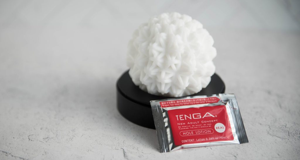 The Tenga GEO sits on the black plastic drying stand without the lid on. The star-like texture is very obvious, and the ball looks extremely plushy and soft. The included lube packet is sitting next to the stroker. For my Tenga GEO review.