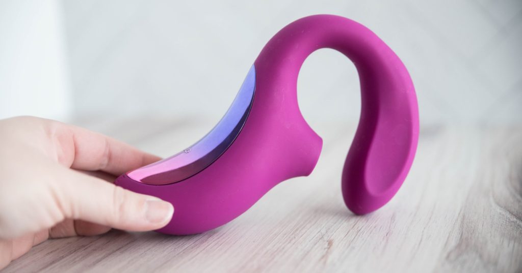 A side view of the LELO Enigma Cruise toy. This showcases the toy's design at rest. It has a protruding air suction tip that works for clitoral stimulation with a g-spot shaft that's flat on the two sides. The plastic, shiny, colorful panel can also be seen in this side view. It is very metallic-looking compared to the flat, matte of the silicone body.