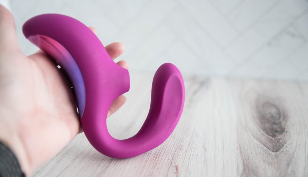 I hold the handle of the LELO Enigma Cruise in my hand while I let the shaft rest on the table. This shows the toy at rest while simultaneously showing that the vibrator's "air suction handle" side is longer than my hand. It looks smaller in pictures than it is in real life.