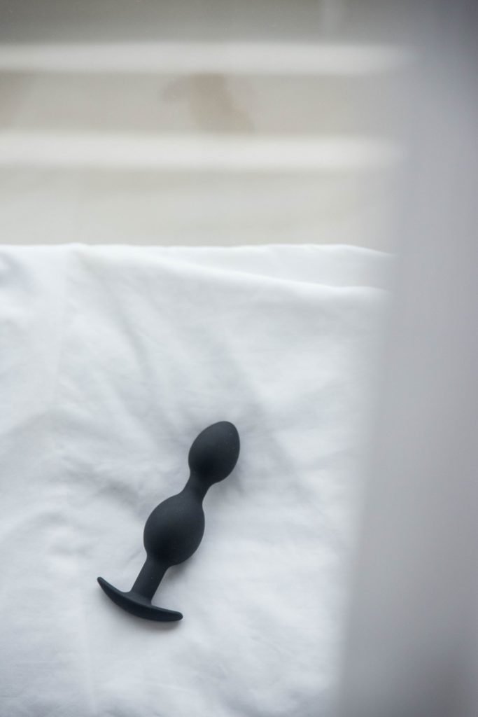 The Holly Fuck II buttplug from MEO.de sitting on a fluffy pillow in front of a window. The soft white curtain is in the foreground, blurred. Natural light evenly lights the entire butt plug, looking sensual. For my Holly Fuck II review.