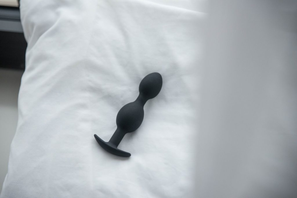 The Holly Fuck II buttplug from MEO.de sitting on a fluffy pillow in front of a window. The soft white curtain is in the foreground, blurred. Natural light evenly lights the entire butt plug, looking sensual. For my Holly Fuck II review.