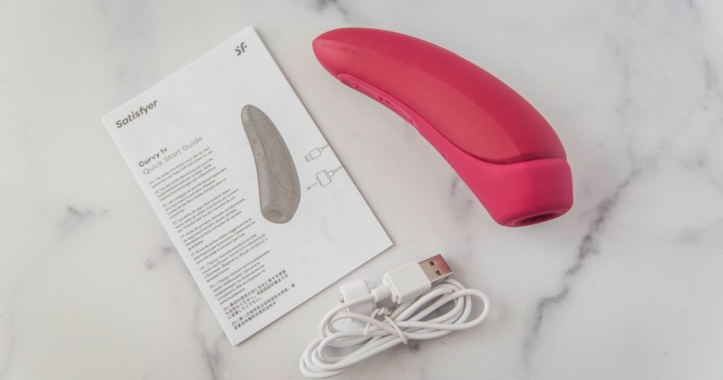 Everything included with the Satisfyer Curvy 1. This shows the instruction manual, the vibrator itself, and the charging cable. For my Satisfyer Curvy 1 review.