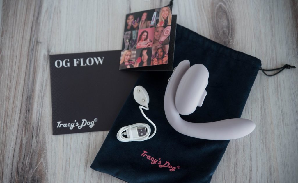 The Tracy's Dog OG Flow and everything included with it. The vibrator lays out on toip of the included blue velvet drawstring bag and the charging cable. The instruction manual and the affiliate information booklet lay next to it. For my Tracy's Dog OG Flow review.
