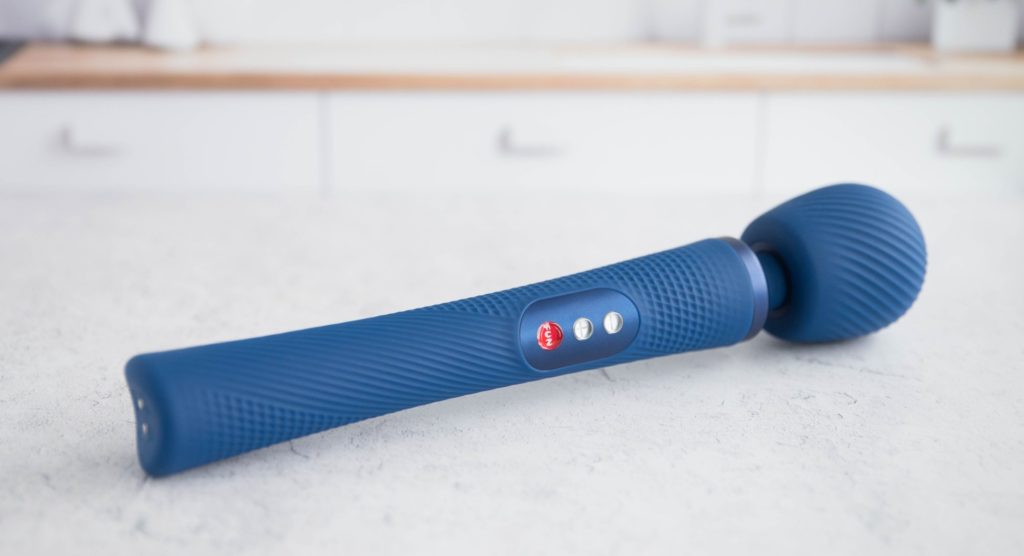 The wand massager laid out on a marbled white surface. The texture is visible all along the wand massager handle and head, and it makes for a very cohesive visual. The wand really stands out compared to the light, white background.