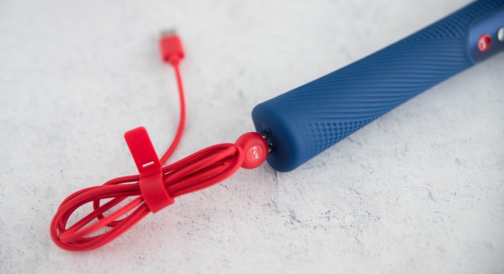 Close up of the magnetic charging cable attached at the base of the wand massager as if it was charging. The other end of the cable, with the USB, is simply laying out on the ground.