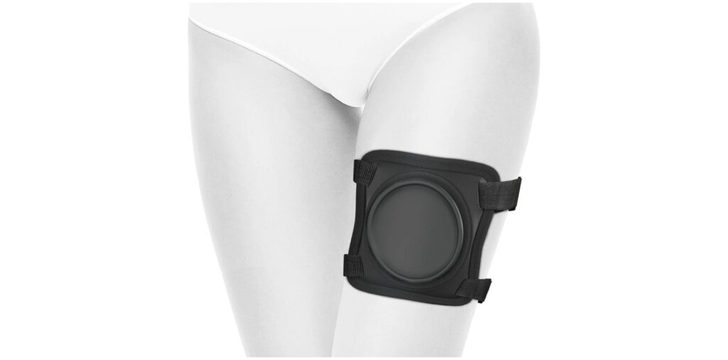 The Body Dock dildo thigh harness wrapped around a leg. It has a large circular platform where suction cup dildos can adhere. 