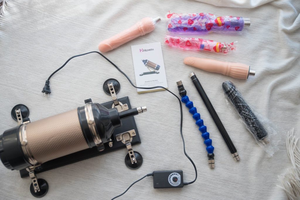 Everything that's included with the 3XLR machine laid out for a top-down photo. There's the machine itself, the power cord with remote built into the cord, the straight extender, the bendable extender, the instruction manual, and the five attachment dildos. For Hismith Sex Machine Review 3XLR version.