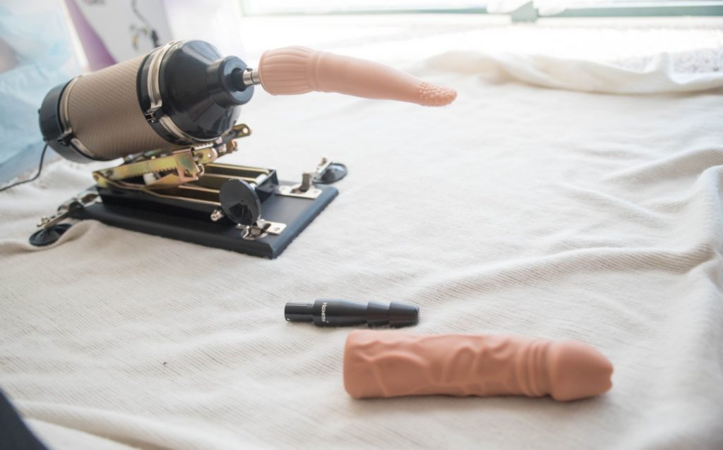 Close-up of an aftermarket accessory I purchased to make the Hismith sex machine work great for us. There's a Vac-U-Lock attachment head shown in the foreground with a silicone Vac-U-Lock dildo in the foreground. The sex machine is shown with a dildo attached in the background. For Hismith Sex Machine Review 3XLR version.