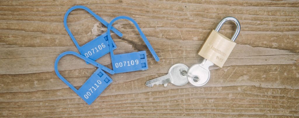 Blue, disposable plastic locks sit out on a wooden surface next to a reusable, metal lock with keys. They're both about the same size.