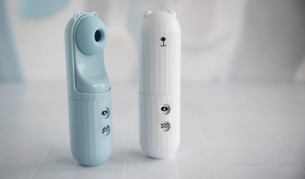 Two MerBear vibrators next to one another. The blue one has the bear panel twisted open to showcase the air suction hole hidden underneath. The white one showcases the closed panel with a bear design on it.