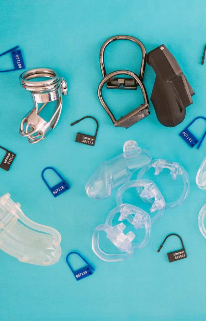 Multiple chastity cages and disposable plastic locks laid out on top of a blue background. Article for my Femdom Locktober Calendar.
