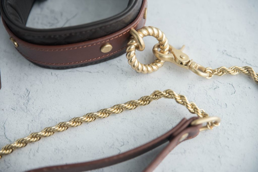 Close-up of all of the gold hardware on the collar and leash. The leash's chain is a braided, circular design. The O-ring has twisted ridges throughout it, and it's relatively thick in size. All of the gold items match in color. For my Liebe Seele Equestrian Leather Collar and Leash review.