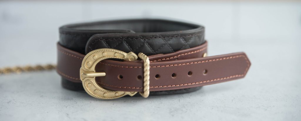 Close-up of the buckle on the back side of the collar. It has a "western" look to it in the same gold hardware as the rest of the collar. It's extremely unique, and it stands out next to the quilted leather look of the collar.