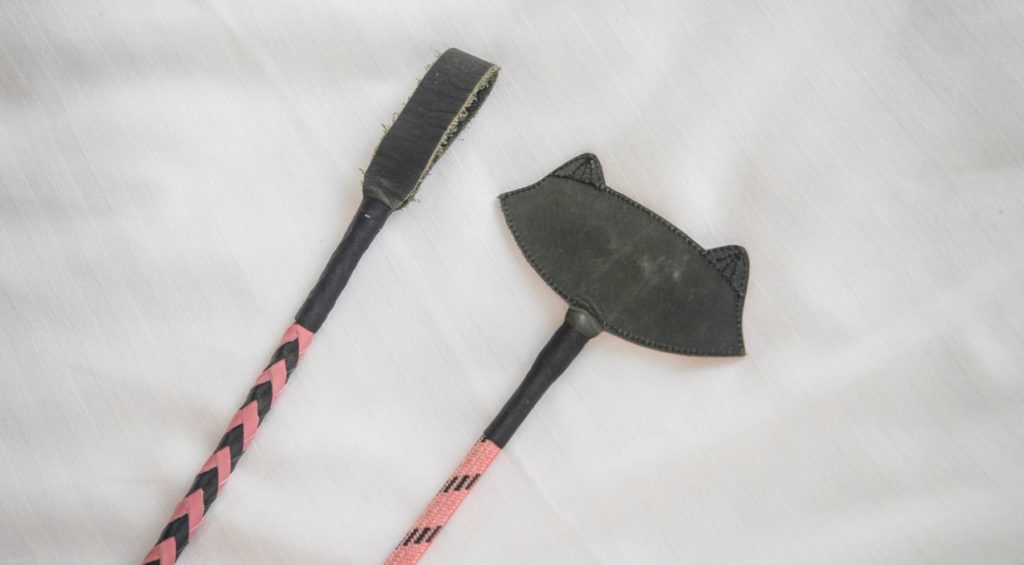 A close-up of two riding crop tips. The crop tip on the left is really small and rectangular. The crop tip on the right is very wide and broad.