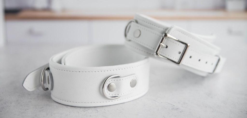 The two cuffs shown on a white countertop with one thigh cuff resting diagonally on top of the other laid-flat cuff. They look beautifully, pure white (not off white) with chromed/silver metal hardware that shines in the light. For my Liebe Seele Fuji White Thigh Cuffs review.