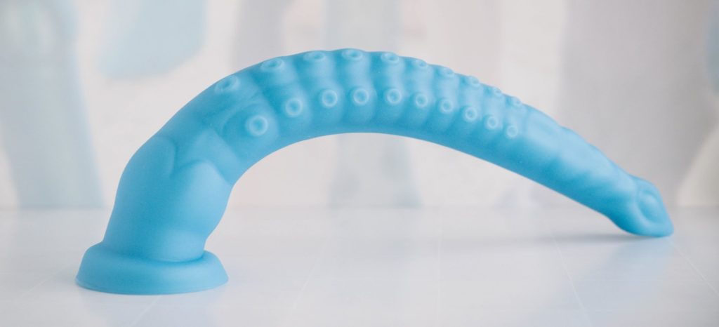 The tentacle dildo is suction cupped to the surface underneath it with the long dildo laying to the side. The suction cup is strong enough to support the weight of the full shaft, and the suction cup stays affixed.