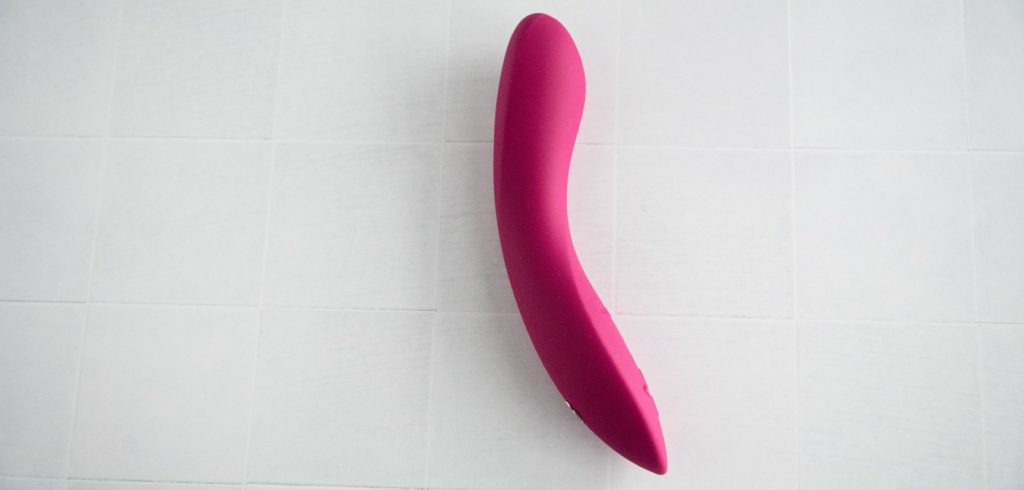 The pink g-spot vibrator laying out on a while tiled background. The Rave 2 is straightened to its neutral state which looks almost straight. Image for my We-Vibe Rave 2 review.