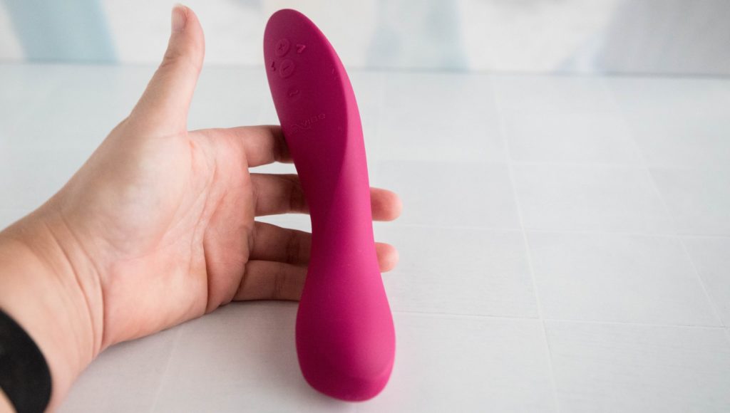 My hand props the vibrator upright at an odd angle, trying to showcase the asymmetrical design of the vibrator. The shaft swirls to the left, making a twirl on the shaft instead of a straight, streamlined shaft. Image for my We-Vibe Rave 2 review.