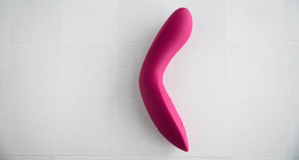 The pink g-spot vibrator laying out on a while tiled background. The Rave 2 is bent to the closest possible angle which is nearing a 90-degree bend. Image for my We-Vibe Rave 2 review.