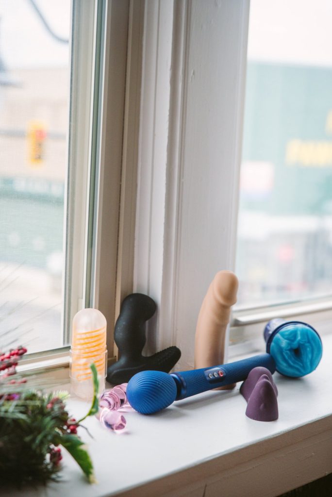 Multiple toys I love rest on a windowsill on a clear and sunny day. They're bright and easy to see. It includes a realistic caucasian dildo, multiple penis strokers, a prostate massager, a glass dildo, a vibrator, and a wand massager.