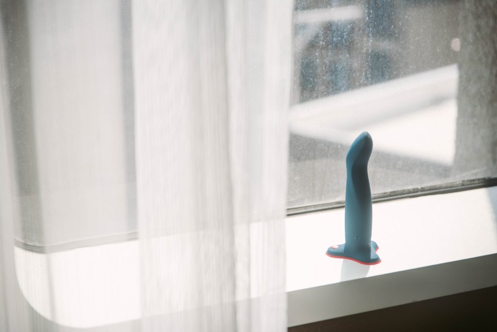The Limba Flex Large dildo sits out on a windowsill. A ton of natural light pours in from the windowsill, and the white, see-through curtains frame the dildo sitting on the ledge. It looks peaceful. For my Fun Factory Limba Flex review.