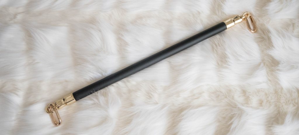 The spreader bar, including its two gold clips, laying out on top of a faux fur blanket. It looks luxurious and soft. Image for my Liebe Seele Black Organosilicon Spreader Bar Review.