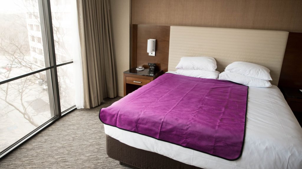 The Aubergine Purple Liberator Throw lays out on a King-sized hotel room bed. It covers about 3/4th of the width of the bed and almost the entirety of the length of the bed. It looks vibrant and welcoming. For my Liberator Throw review.