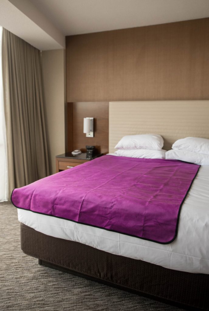 The Aubergine Purple Liberator Throw lays out on a King-sized hotel room bed. It covers about 3/4th of the width of the bed and almost the entirety of the length of the bed. It looks vibrant and welcoming. For my Liberator Throw review.