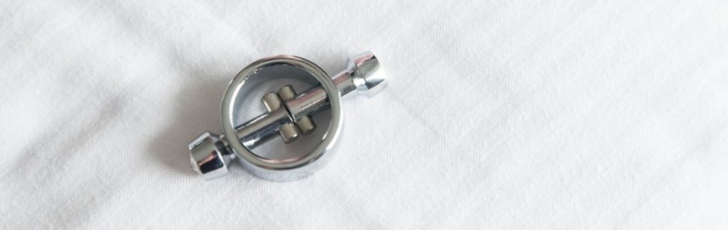 A magnetic nipple clamp sitting at-rest on top of a white bedspread.