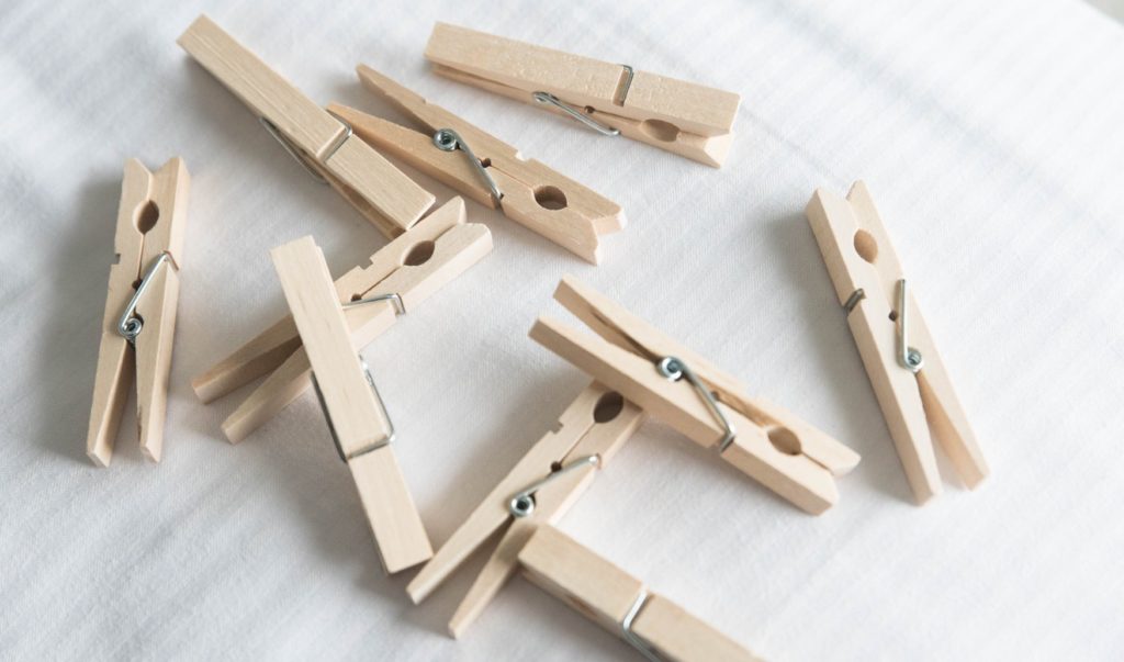 A pile of plain clothespins laid out on a white bedspread, piled on top of one another. For my BDSM Nipple Clamps article.