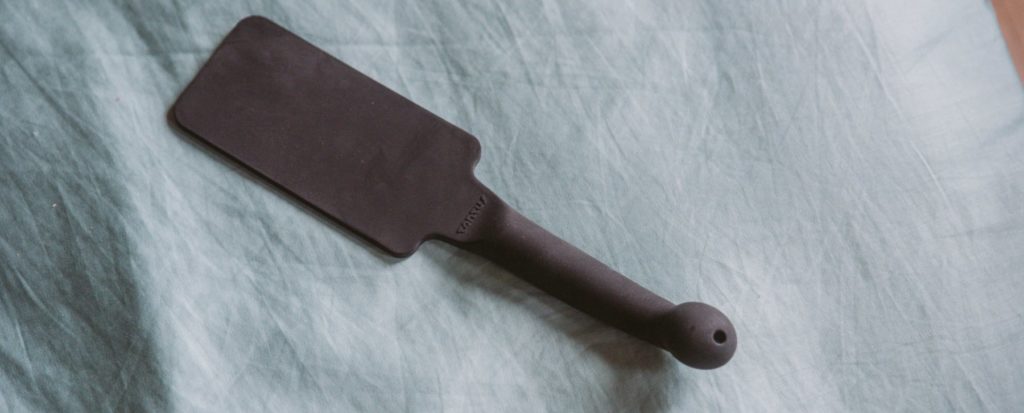 A silicone paddle from Tantus just laying on a blue bedspread. For my Everything You need to Know about Using a BDSM Paddle review.
