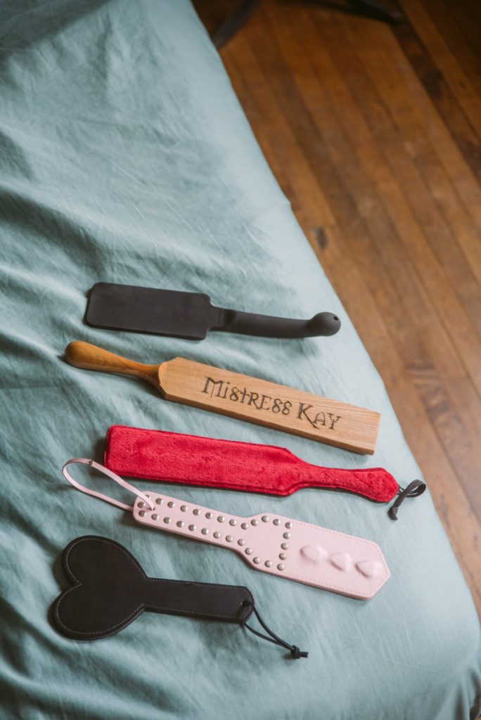 A spread of kinky paddles laying out the blue bedspread, showcasing their different sizes and colors and styles. For my Everything You need to Know about Using a BDSM Paddle review.