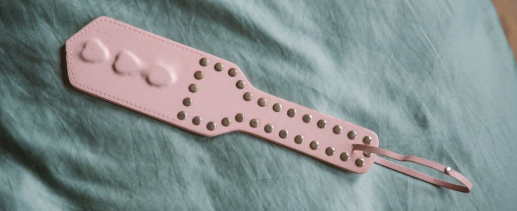 A pink PVC paddle, laying on top of a blue bedspread.