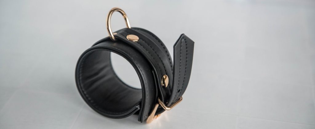 The cuff is rolled into a circle and shown fastened. There's a lot of excess strap hanging off the cuff. The D-ring is shown protruding far away from the cuff, not resting up against the cuff.