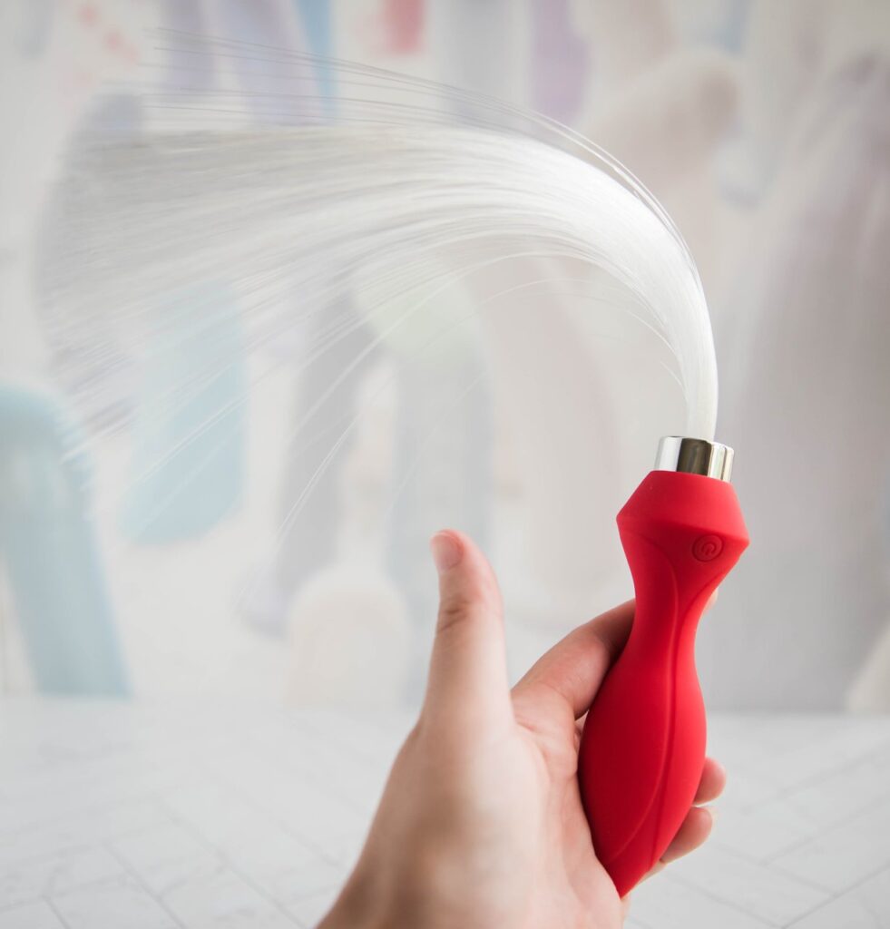 My hand holds onto the Inyarose vibrator, facing the toy's base up to the ceiling. The fiber optic tails drape in a U-shape from being stored in a U-shape inside of the packaging for so long. They do not straighten out straight.