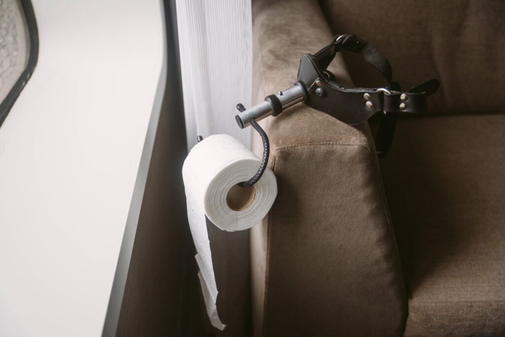 The gag with attached toilet paper attachment hangs off a chair, holding a toilet paper roll. Image for my Getting Ready for a Femdom Date BDSM Scene